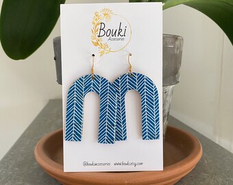 May include: A pair of blue and white chevron patterned arch-shaped earrings with gold hooks. The earrings are displayed on a white card with the text "Bouki Accessories" and the social media handles @boukiaccessories and www.boukietsy.com.