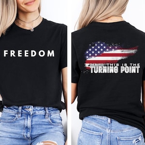 Peut inclure: T-shirt noir avec le mot "FREEDOM" en lettres blanches sur le devant. Le dos du t-shirt présente un motif de drapeau américain vieilli avec le texte "THIS IS THE TURNING POINT". Le t-shirt est associé à un jean bleu.