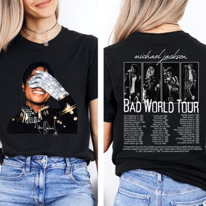 May include: A black t-shirt featuring a front graphic of Michael Jackson wearing a sequined glove over his face and a back graphic with four black and white photos of the artist, the text "michael jackson BAD WORLD TOUR," and a list of tour dates.