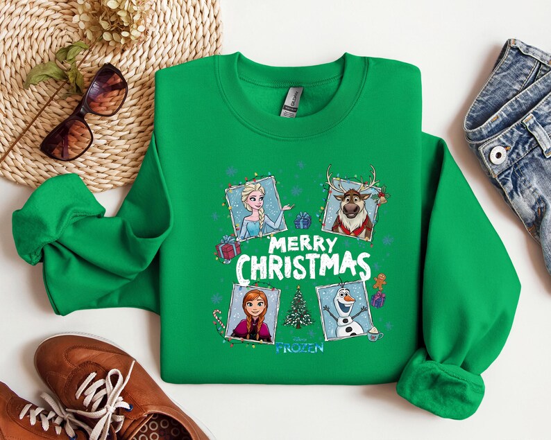 Puede incluir: Una sudadera verde de cuello redondo con un dise&ntilde;o festivo con personajes de la pel&iacute;cula Frozen. El dise&ntilde;o incluye a Elsa, Anna, Olaf y Sven, con las palabras "Merry Christmas" en blanco. La sudadera tiene mangas largas y pu&ntilde;os acanalados.