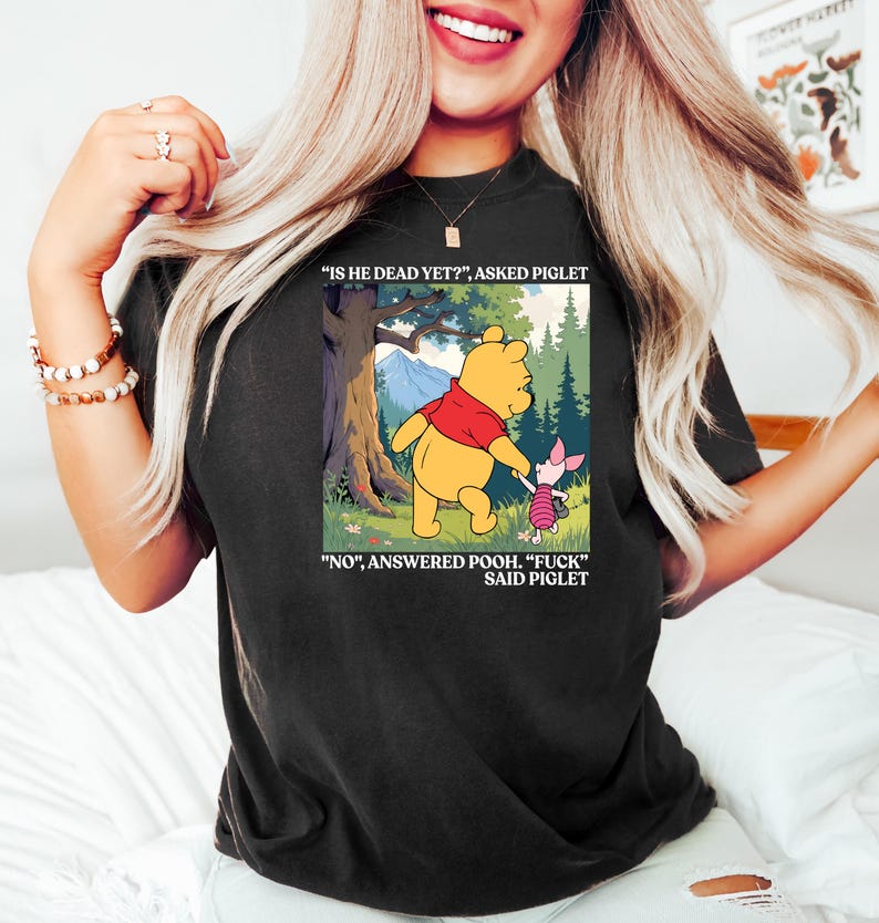 Puede incluir: Camiseta negra con una imagen de dibujos animados de Winnie the Pooh y Piglet. La imagen incluye el texto "IS HE DEAD YET?" y "NO", ANSWERED POOH. "FUCK" SAID PIGLET". Es una prenda informal.