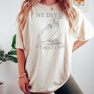 May include: A cream colored oversized t-shirt with a black and white illustration of a bird and the text "Ni Dieu Ni Maitre".