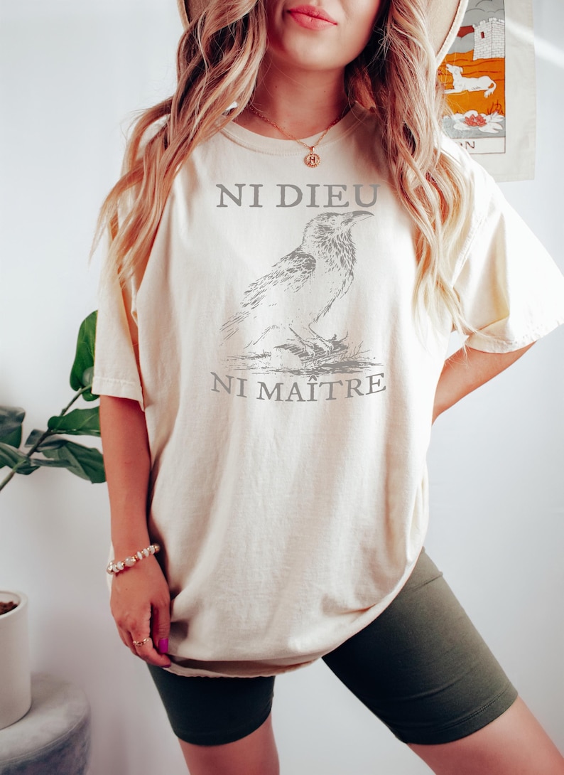 May include: A cream colored oversized t-shirt with a black and white illustration of a bird and the text "Ni Dieu Ni Maitre".