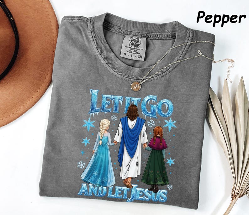May include: A gray Comfort Colors t-shirt with the phrase "LET IT GO AND LET JESUS" in blue and white. The graphic features Jesus, Elsa, and Anna. A silver necklace is draped across the shirt.