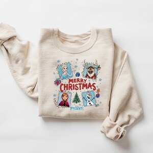 Puede incluir: Sudadera beige de cuello redondo con personajes de la pel&iacute;cula Frozen. El dise&ntilde;o incluye a Elsa, Anna, Olaf y Sven, con las palabras "Merry Christmas" y "Frozen". Una prenda festiva y c&oacute;moda.