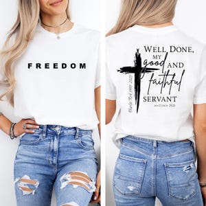 May include: White t-shirt with the word "FREEDOM" in black block letters on the front. The back of the shirt features a black cross design with the words "Well Done, My Good and Faithful Servant" and the text "Matthew 25:21".