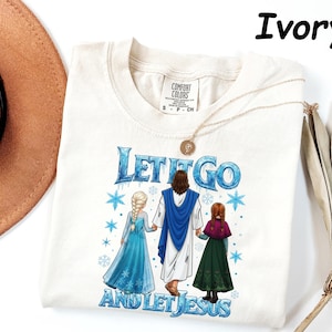May include: Ivory-colored t-shirt featuring the text "LET IT GO AND LET JESUS" in blue, with illustrations of Jesus and two characters from the movie Frozen. The shirt has a crew neck and short sleeves.
