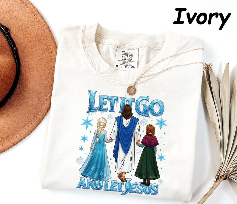 May include: Ivory-colored t-shirt featuring the text "LET IT GO AND LET JESUS" in blue, with illustrations of Jesus and two characters from the movie Frozen. The shirt has a crew neck and short sleeves.