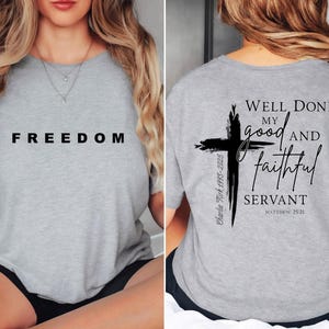 May include: A light grey t-shirt with the word "FREEDOM" printed in black on the front. The back of the shirt features a black cross design with the text "Well Done, my good and faithful servant" and the Bible verse Matthew 25:21.