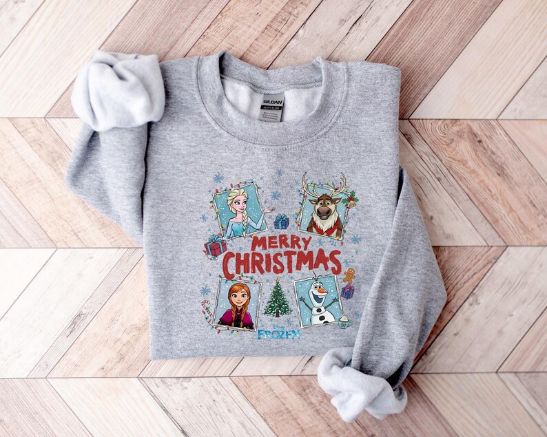 Puede incluir: Una sudadera gris con personajes de la pel&iacute;cula Frozen, incluyendo a Elsa, Anna, Olaf y Sven, con las palabras "Merry Christmas" y "Frozen" impresas en la parte delantera. La sudadera es de un material suave.