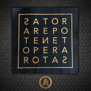 May include: A black fabric patch with a gold square frame containing the letters "ZATOR AREPO TENET OPERA  ROTAZ".