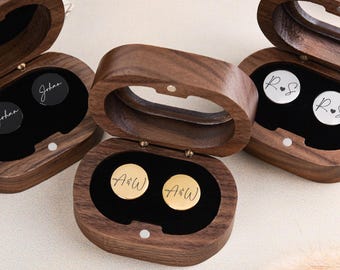 May include: Three wooden cufflink boxes, each with a hinged lid, are open to reveal personalised cufflinks. The cufflinks are round, with black, silver, and gold finishes. The cufflinks are engraved with initials and names.