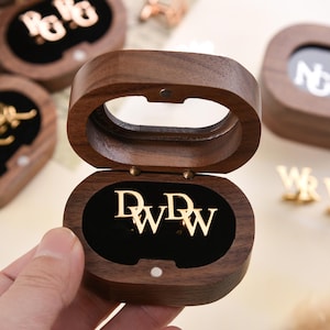 May include: Wooden jewellery boxes with gold-coloured initial earrings inside. The boxes are open, revealing the earrings against a black velvet interior. Other boxes with initials are in the background.