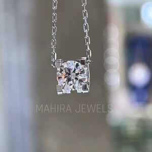 Puede incluir: Un collar de cadena de plata con un gran colgante redondo de diamante transparente engastado en un marco cuadrado.