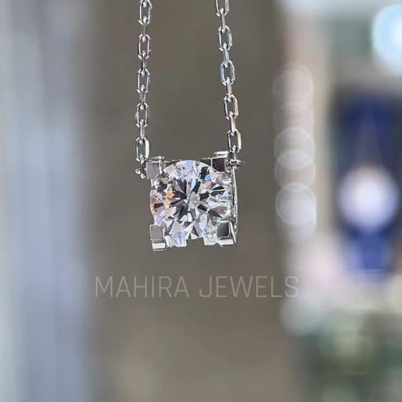 Puede incluir: Un collar de cadena de plata con un gran colgante redondo de diamante transparente engastado en un marco cuadrado.