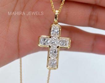 Puede incluir: Un collar con colgante de cruz en oro con cinco piedras claras rectangulares de corte radiante dispuestas en forma de cruz, con el texto MAHIRA JEWELS impreso en la esquina superior izquierda. El colgante cuelga de una fina cadena de oro.