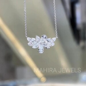May include: A silver necklace featuring a floral pendant design. The pendant is composed of multiple clear, sparkling gemstones, with a central pear-shaped stone. The necklace is delicate and elegant, suitable for special occasions. The text "MAHIRA JEWELS" is visible.
