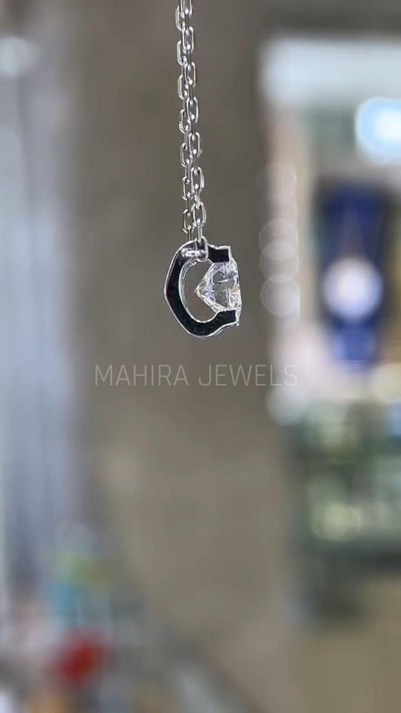 Puede incluir: Un collar de cadena de plata con un colgante de piedra preciosa transparente en forma de letra C. El colgante est&aacute; engastado en un marco de plata.