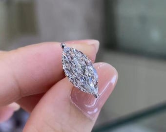 May include: A marquise-cut diamond gemstone, held between fingers. The diamond is clear and faceted, reflecting light. The setting appears to be a simple, delicate metal. The overall impression is of a high-quality, elegant piece of jewellery.