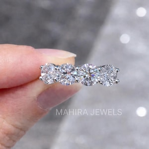 Könnte beinhalten: Nahaufnahme eines silbernen Rings mit vier runden, klaren Edelsteinen. Der Ring wird von einer Hand gehalten. Der Text "MAHIRA JEWELS" ist unten im Bild zu sehen.