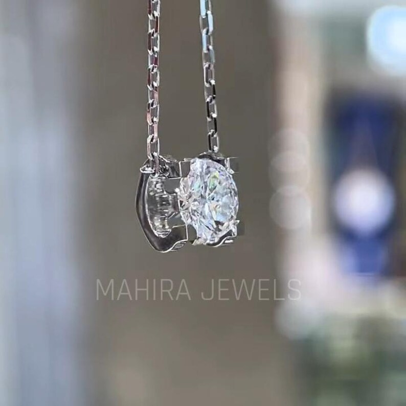 Puede incluir: Un collar de cadena de plata con un gran colgante redondo de piedra preciosa transparente. El colgante est&aacute; engastado en un marco de plata con un dise&ntilde;o delicado. El collar est&aacute; colgado sobre un fondo borroso.