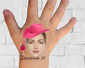 Può includere: Una mano con una sovrapposizione digitale di un cappello da cowboy rosa, il volto di una donna e una grafica di cocktail. Il testo "Susana 21" è sotto il volto e la parola "TATTOO" è in basso.