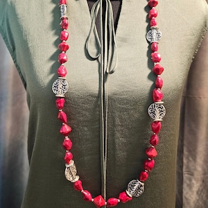 May include: A long necklace featuring large, faceted red beads interspersed with ornate silver-toned metal accents. The necklace is displayed on a mannequin, showcasing its length and design. The beads have an irregular shape, adding to the necklace's unique appeal.