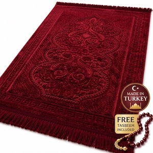May include: A deep red prayer rug with an ornate central design and a geometric border. The rug has a fringed edge and a textured surface. A tag indicates it is made in Turkey. A set of prayer beads is included.
