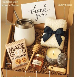 May include: A gift box filled with various items, including a white tumbler with a straw, a small bag of chocolate chip granola, a jar of honey with a honey dipper stick, a white fluffy sock with a black ribbon, a small scented candle in a blue and white ceramic container, a leather keychain, and a personalised card that says "thank you".