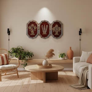 Puede incluir: Salón con una combinación de colores beige claro. Tres tapices de pared enmarcados con diseños dorados y rojos están encima de una estantería de madera. Una silla de ratán con un cojín a rayas y un sofá beige están en la habitación.