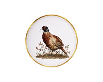 May include: A round white plate with a gold rim featuring a detailed illustration of a pheasant standing on a patch of ground with small plants. The bird has brown, tan, and black feathers with a dark head and a red patch around the eye.