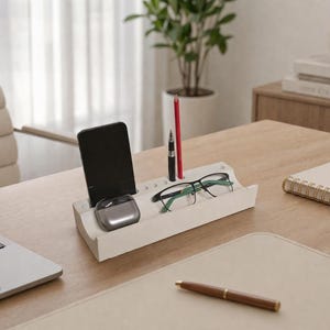 Może przedstawiać: Biały organizer biurkowy mieści czarny smartfon, srebrne słuchawki i okulary w zielonych oprawkach. Czerwony ołówek i czarny długopis stoją pionowo. Na jasnym drewnianym biurku znajduje się również laptop, notatnik i długopis.