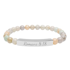 May include: A stretch bracelet featuring smooth, multi-colored pastel stone beads in shades of cream, peach, and soft green. A polished silver-tone metal bar is centered on the strand, engraved with the text Romans 8:18 in a cursive font.