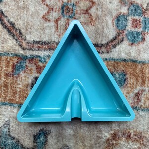 Puede incluir: Un cenicero triangular de color azul claro con una superficie lisa.
