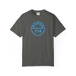 May include: Dark grey t-shirt with a blue circular graphic. The graphic features the word "RORER" above the number "714" in a blue, sans-serif font. The shirt is a short-sleeved, crew neck style.