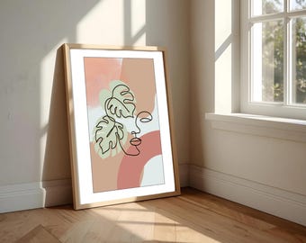 Op de afbeelding: Een ingelijste kunstdruk met een minimalistische lijntekening van een gezicht en monstera bladeren. Het kunstwerk staat tegen een achtergrond van perzik, roze en witte vormen. De lijst is van licht hout.