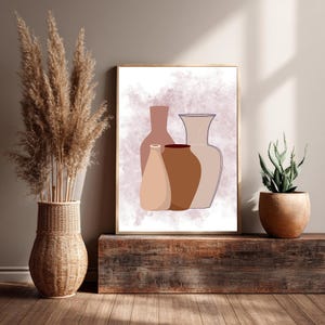May include: A framed art print featuring a minimalist illustration of four vases in shades of brown and beige against a soft, watercolor-like background. The artwork is displayed on a rustic wooden surface, alongside a woven vase with dried pampas grass and a potted succulent.