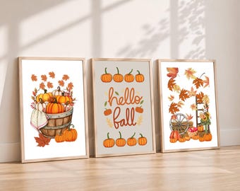 May include: Three framed wall art prints featuring autumn themes. The left print shows a wooden barrel filled with orange and white pumpkins. The center print displays the text hello fall with orange pumpkins. The right print depicts a wagon wheel.