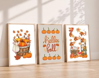 May include: Three framed wall art prints featuring autumn themes. The left print shows a wooden barrel filled with orange and white pumpkins. The center print displays the text hello fall with orange pumpkins. The right print depicts a wagon wheel.