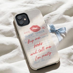 May include: A phone case with a printed design resembling a guest check. It features a red lipstick kiss, hearts, and the text "Buy me books and tell me I'm pretty." A light blue ribbon is tied to the side.
