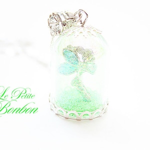 May include: A silver pendant necklace with a glass dome containing a green glitter fairy figurine. The pendant is labeled "Le Petite Bonbon".