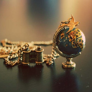 Around the world golden bird on the Globe with binocular necklace