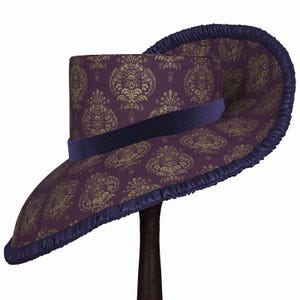 May include: A wide-brimmed hat with a purple and gold damask pattern. The hat has a dark blue velvet band and a ruffled edge.