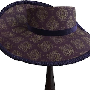 May include: A wide-brimmed hat with a purple and gold paisley pattern. The hat has a dark purple velvet band and a ruffled edge.