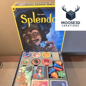 May include: An open Splendor board game box, showing the game's contents. The box art features a man holding a gem. Inside, a gray tray organises cards, tokens, and wooden pieces. The game includes cards, tokens, and wooden pieces.