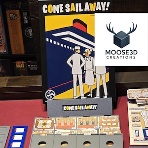 May include: The board game "Come Sail Away!" is displayed, showcasing a vintage cruise ship illustration. The game includes grey game boards, cards, and tokens. The logo "MOOSE3D CREATIONS" is visible. The game's title is also printed on the game boards.