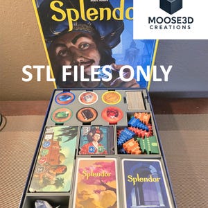 Puede incluir: Caja del juego de mesa "Splendor" con el texto "STL FILES ONLY". La caja abierta revela cartas, fichas y piezas del juego. La ilustración de la caja presenta un retrato de un hombre. Diseñado por Marc André.