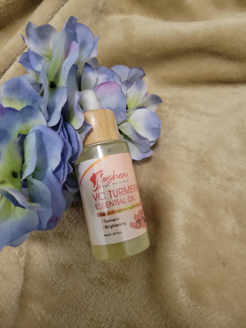 May include: A clear glass bottle with a bamboo dropper and a white label that says "Goshen Skin Science VC Turmeric Essential Oil" with the text "VC Brightening & Firming" and "Turmeric Brightening" in smaller font. The bottle is sitting on a brown fuzzy surface.