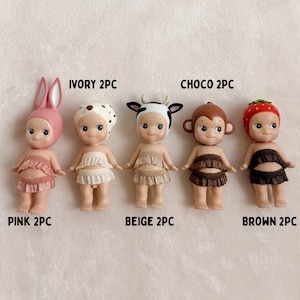 Puede incluir: Cinco peque&ntilde;as figuras con sombreros y trajes con tem&aacute;tica de animales. Las figuras son de color rosa, marfil, beige, marr&oacute;n y chocolate. Cada figura tiene una parte superior e inferior con volantes. El texto de la imagen dice "PINK 2PC", "IVORY 2PC", "BEIGE 2PC", "CHOC 2PC" y "BROWN 2PC".