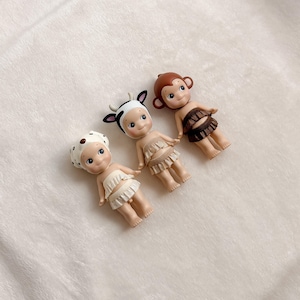 Puede incluir: Tres peque&ntilde;as figuras decorativas. Una es una vaca, otra es un mono y otra es un d&aacute;lmata. La figura de la vaca tiene un sombrero con estampado de vaca en blanco y negro con cuernos negros. La figura del mono tiene una cabeza marr&oacute;n y una falda marr&oacute;n. La figura del d&aacute;lmata tiene un sombrero blanco con manchas marrones.